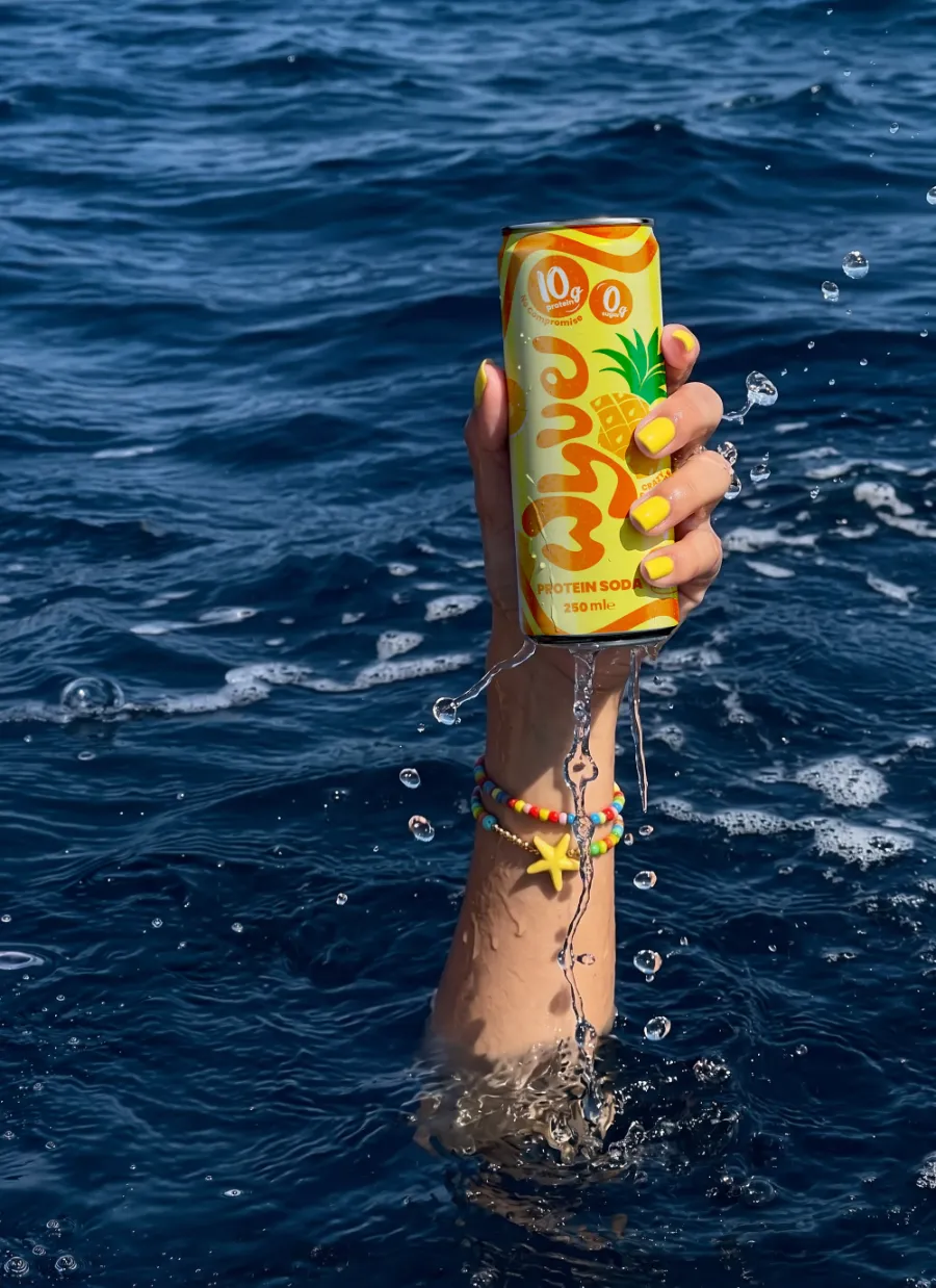 An arm rising out of deep blue open sea, water streaming off it, holding a WYVE Crazy Pineapple can above the surface